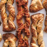 Close-up of golden-brown twisted pastries sprinkled with coarse sugar on a light background.