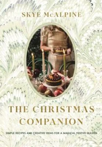91BW9Ga+2AL_SL1500_ Book cover for The Christmas Companion by Skye McAlpine; an oval photo shows a woman in a gold dress holding a cake, set on a marbled pastel background.