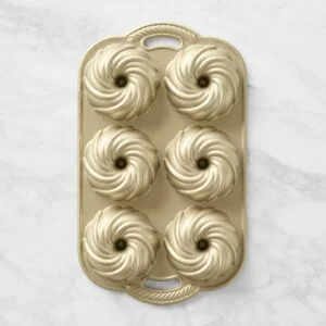 nordic-ware-nonstick-cast-aluminum-swirl-bundtlette-cake-p-xl Gold silicone baking mold with multiple swirl-shaped pastry cavities arranged in a grid on a light marble surface