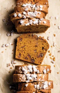 Sliced nutty loaf cake with walnuts and a light dusting of powdered sugar on parchment